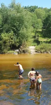 three people standing in the water in a river at La Ribera Hotel Dormis Camping in Villa Carlos Paz