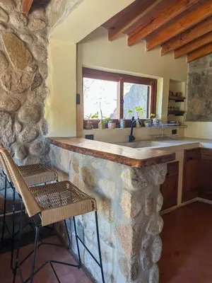 a kitchen with a stone counter and chairs in a room at Casa de piedra con jardin y pileta - privada in Los Hornillos