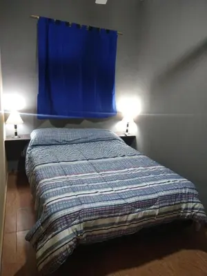 a bedroom with a bed with a blue curtain and two lamps at Lo de Andrés y Marina in Arroyo de Los Patos