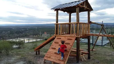 a young boy is climbing up a wooden playground at Estancia de Campo in Estancia Vieja