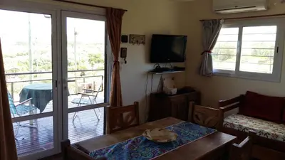 a living room with a table and a television and a balcony at Estancia de Campo in Estancia Vieja