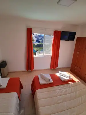 a room with two beds and a window with red curtains at HOTEL CRISTAL in Villa Carlos Paz