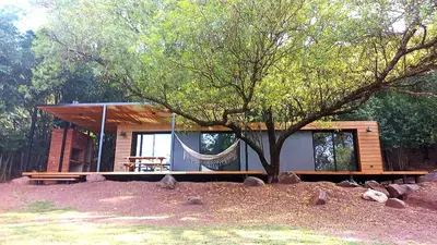 a log cabin with a hammock in front of it at Casa Container Embalsina Villa del Dique in Villa del Dique