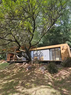 a tiny house sitting under a tree in a field at Casa Container Embalsina Villa del Dique in Villa del Dique