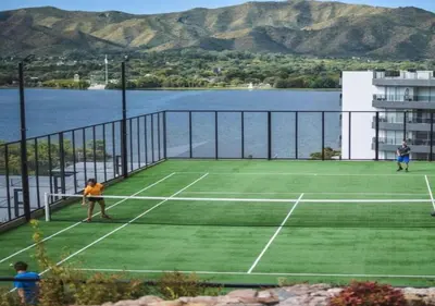 two people playing tennis on a tennis court next to the water at Veneto Village - Vista al Lago - 10 minutos a Carlos Paz in Villa Parque Siquiman