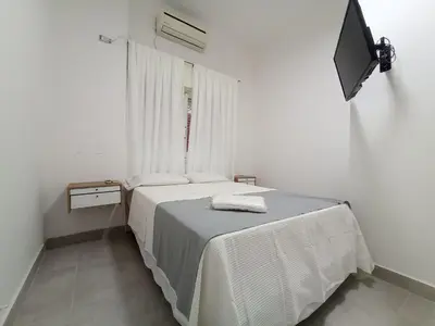 a white bedroom with a bed and a television at Artigas Confort - Bienes Reales in Cordoba