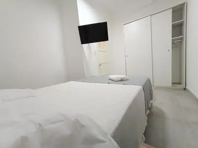a white bedroom with two beds and a flat screen tv at Artigas Confort - Bienes Reales in Cordoba