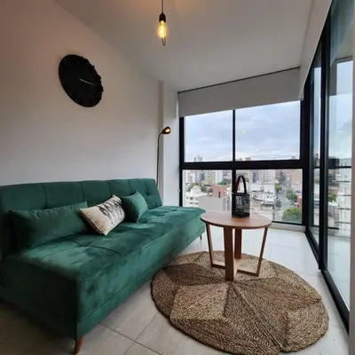 a green couch in a living room with a clock on the wall at Loft en Güemes Piso 9 in Cordoba