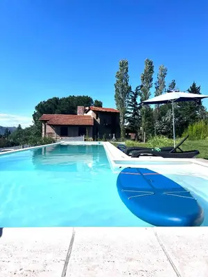 a blue swimming pool with an umbrella and chairs at Lago de montaña in Villa Carlos Paz