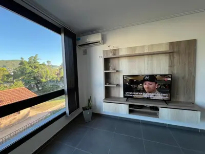a living room with a tv and a large window at Edificio Stefano III - Departamento con cochera y amenities a pocas cuadras del centro in Villa Carlos Paz