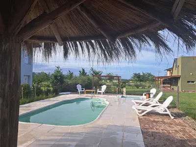 a swimming pool with chairs and a straw umbrella at Cabañas Aires De Luna in Los Reartes