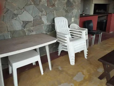 two white chairs and a wooden table in front of a stone wall at Paraíso Serrano 16 in Villa Ciudad Parque
