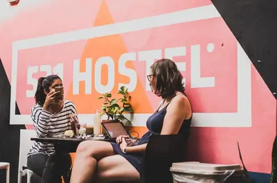 two women sitting at a table in front of a wall at 531 Hostel in Cordoba
