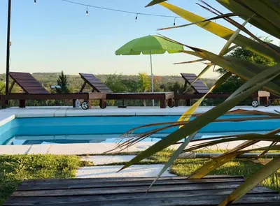 a swimming pool with benches and a green umbrella at Cabaña Snowflakes in Villa Yacanto
