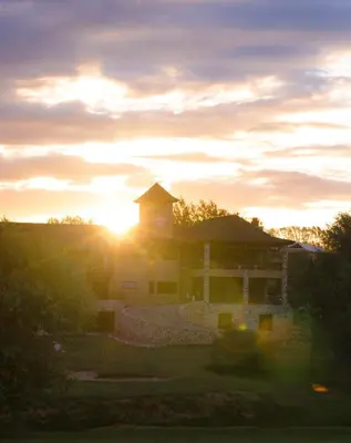 a building with the sun setting in the background at Ayres del Champaqui Hotel Boutique Experiencial & Spa in Villa General Belgrano