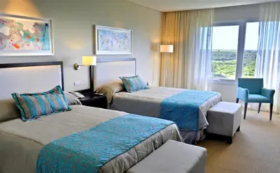 a hotel room with two beds and a chair at Howard Johnson Hotel Piedras Moras in Almafuerte