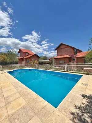 a blue swimming pool in front of two houses at Cabañas Abril in Merlo