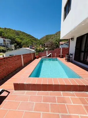 a swimming pool next to a building with a brick wall at Departamentos Pasini in Villa Carlos Paz