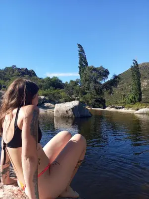 two girls sitting on the shore of a river at la balsa in Mina Clavero