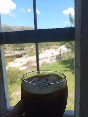 a glass of coffee sitting in front of a window at la balsa in Mina Clavero