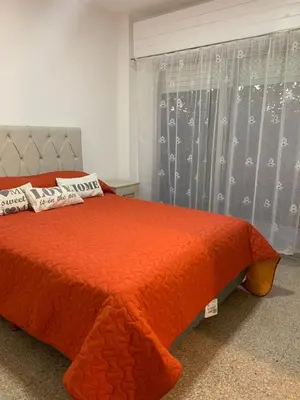 a bed with an orange comforter and a window at Departamento Costanera in Villa Carlos Paz