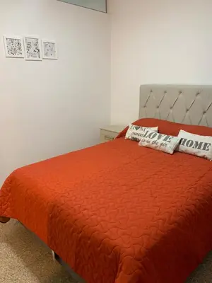 a bed with an orange comforter and two pillows on it at Departamento Costanera in Villa Carlos Paz