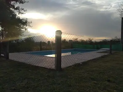 a fence around a swimming pool with the sun behind it at Cabaña Malibu in Los Reartes