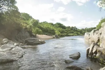 a river with rocks and trees in the background at Cueva de lujo con rio de montaña Casa cueva in Villa Cura Brochero