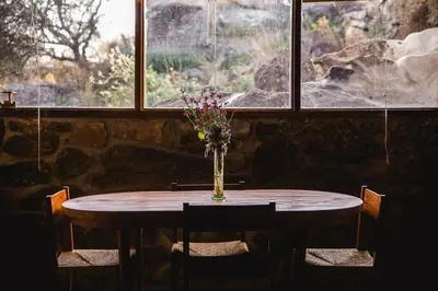 a table with a vase of flowers on it in front of a window at Cueva de lujo con rio de montaña Casa cueva in Villa Cura Brochero