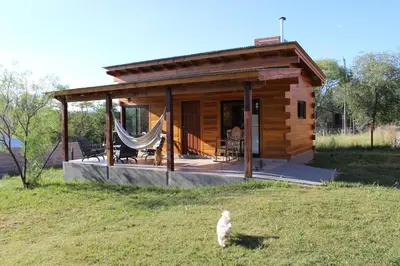a small log cabin with a cat standing in the grass at Los Grillos Cabañas Serranas in Los Reartes