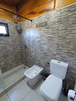 a bathroom with a white toilet and a shower at Los Grillos Cabañas Serranas in Los Reartes