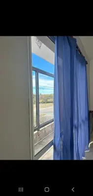 a window with a blue curtain looking out at an airport at Depto por día in Río Cuarto