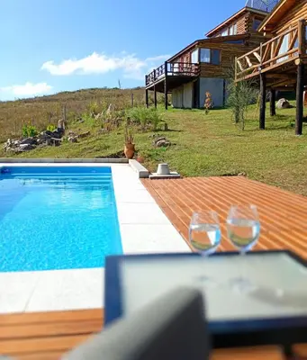 two wine glasses sitting on a table next to a swimming pool at La Autóctona in Villa Yacanto