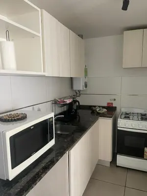 a white kitchen with a microwave and a stove at CATEGORIA departamento a dos cuadras del patio olmos 1 dormitorio asador pileta y cochera in Cordoba