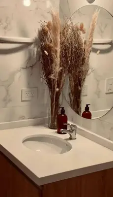 a bathroom sink with a mirror and a vase with dried plants at Depto Villa Carlos Paz in Villa Carlos Paz