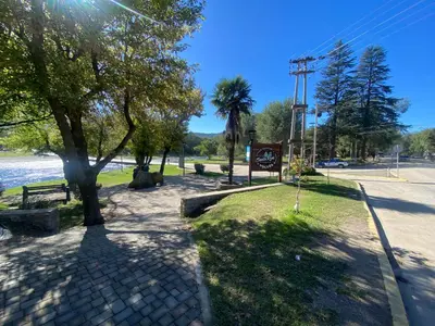 a park with trees and a sidewalk next to the water at Departamentos Altos del Puchuqui in Santa Rosa de Calamuchita