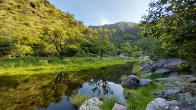 a river with rocks and trees and a mountain at Cabañas MACONDO in Villa Ciudad Parque