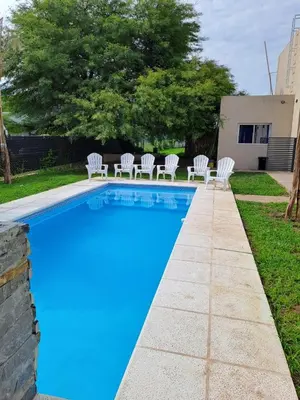 a blue swimming pool with white chairs next to a yard at Baumhaus in Villa Anizacate