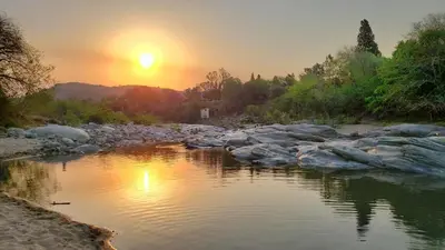 a river with the sun setting in the background at Baumhaus in Villa Anizacate