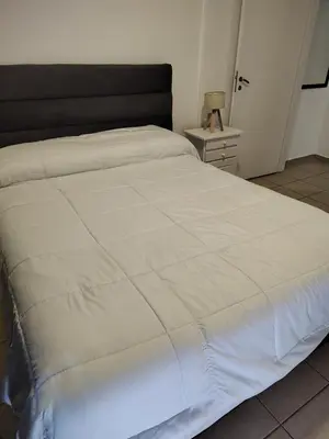 a large white bed in a bedroom with a night stand at Dpto Nuevocentro Shopping CON ESTACIONAMIENTO GRATUITO in Cordoba