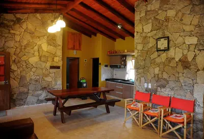 a kitchen with a table and chairs and a stone wall at Complejo Terrazas al Champaqui in Villa Yacanto