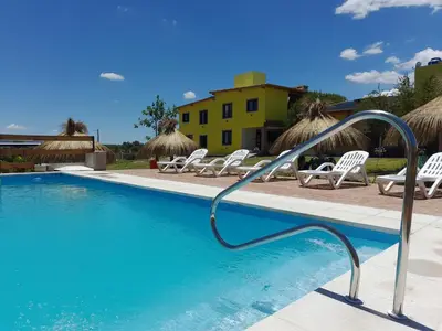 a swimming pool with white chairs and umbrellas at Cabañas R&E in Mina Clavero
