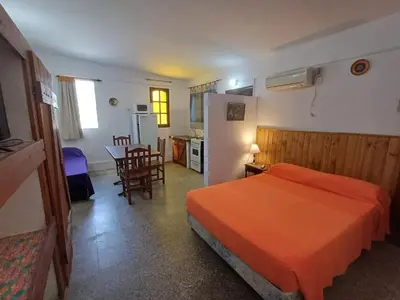 a bedroom with a bed and a kitchen and a table at Los Luises - Departamentos Céntricos in Mina Clavero