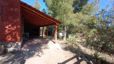 a covered porch of a red house with trees at Al Pie Del Cerro Champaqui in Los Hornillos