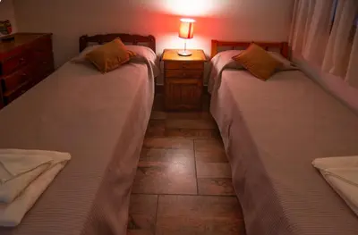 two beds in a bedroom with a lamp on a table at La Chuklla, alojamiento cerca al lago in Almafuerte