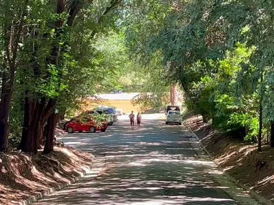 two people walking down a road with cars and trees at Las Magnolias - Casas de Campo in Mina Clavero