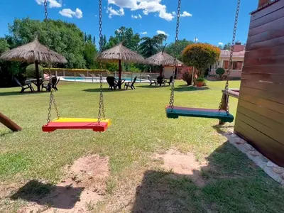 three swings in a yard with chairs and umbrellas at Las Magnolias - Casas de Campo in Mina Clavero