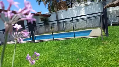 a fence with a pool in a yard with purple flowers at Complejo Luluara in Villa Carlos Paz