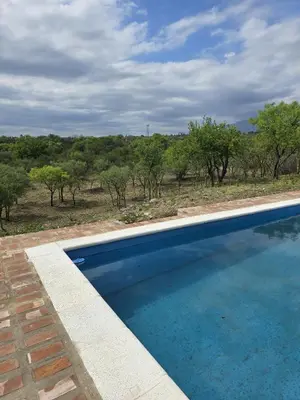 a swimming pool in front of a field with trees at El Alto in Yacanto