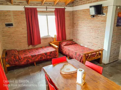 a room with two beds and a table and a window at Cabañas El Cardón in Santa Rosa de Calamuchita
